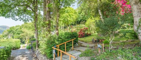 A stone staircase leading up to a wooden deck surrounded by lush greenery and flowering plants.