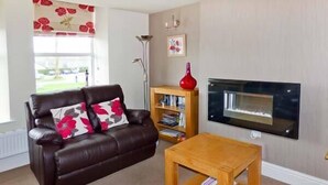A living room with a brown leather sofa, a wooden coffee table, a bookshelf, and a fireplace. - Swallows Nest (Coniston)