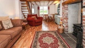A cozy living room with a wooden floor, a red sofa, a patterned rug, and a fireplace. - The Cottage (Driffield)