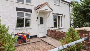 A white two-story house with a front door, two windows, and a small porch area with a colorful blanket. - The Cottage (Driffield)