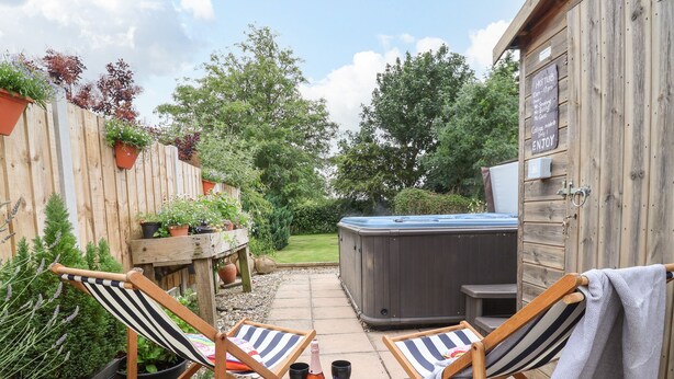A patio area with two striped lounge chairs, a hot tub, and a wooden deck. - The Cottage (Driffield)