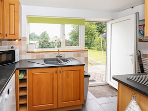 A modern kitchen with wooden cabinets, a black countertop, a double sink, and a window with a view of a garden.