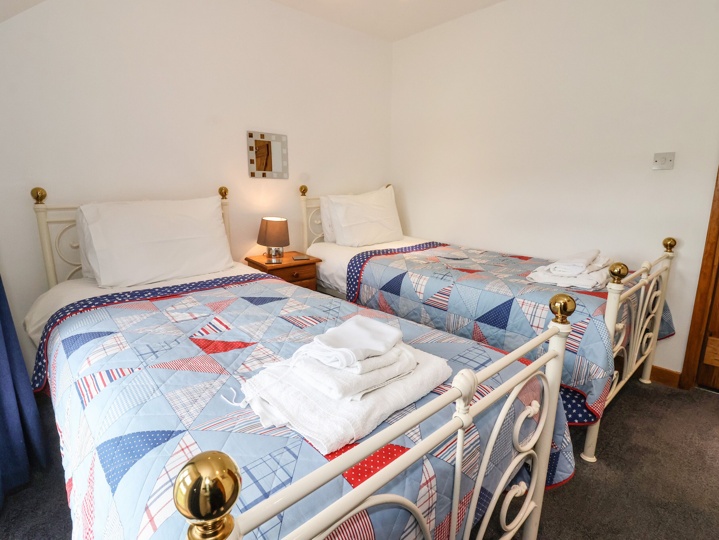 Una habitación con dos camas, cada una con un edredón acolchado con motivos patrióticos. Hay una mesita de noche con una lámpara entre las camas, y un reloj de pared encima de la mesita.