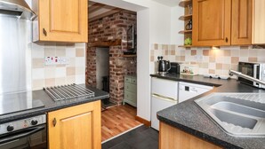 A compact kitchen with wooden cabinets, a built-in oven, a dishwasher, and a microwave. - The Cottage (Driffield)
