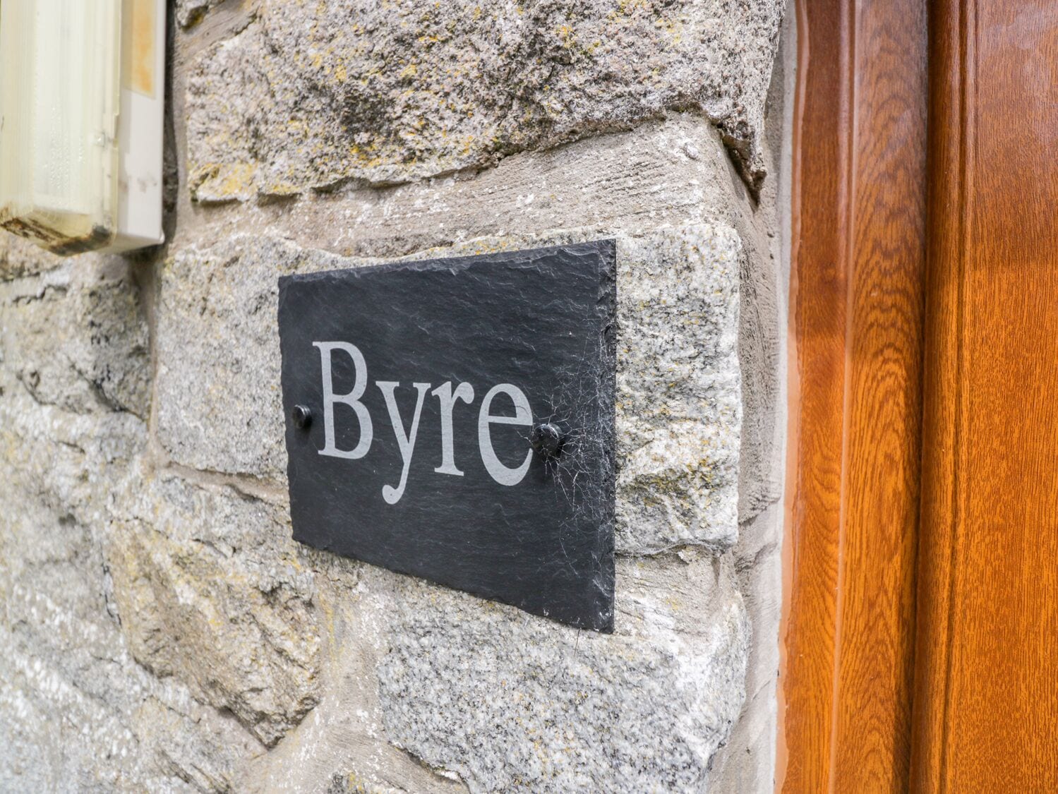 A stone wall with a black slate sign that reads "Byre."