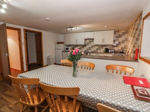 A dining area with a round table covered in a polka dot tablecloth, surrounded by wooden chairs. A vase with flowers is placed on the table. - The Byre (Newton Stewart)