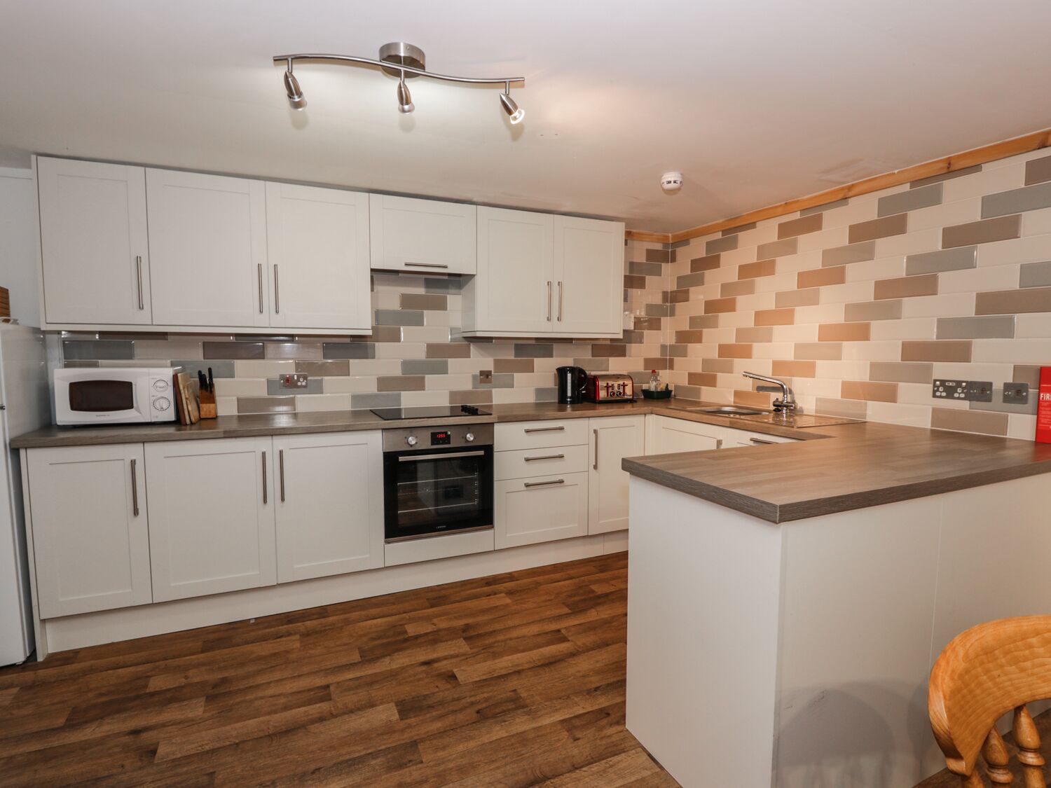 A modern kitchen with white cabinets, a microwave, an oven, and a wooden countertop.