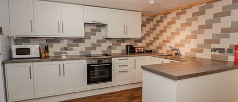 A modern kitchen with white cabinets, a microwave, an oven, and a wooden countertop.