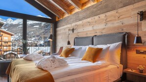 Ein Schlafzimmer mit einem großen Bett, einem Holzkopfende und Blick auf einen verschneiten Berg.