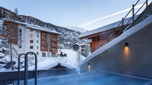 Ein Wellnessbereich mit Whirlpool, Holzhäusern und einem verschneiten Bergpanorama.