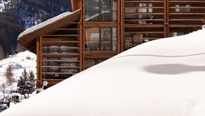 A wooden chalet with large windows and a snow-covered roof, set against a backdrop of snow-capped mountains and a clear sky. - 22 Summits Boutique Hotel (Zermatt)