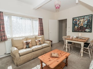 Un salon chaleureux avec un canapé, une table basse en bois, une table à manger avec des chaises et un tableau accroché au mur.