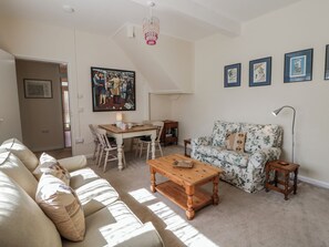 Un salon comprenant un canapé, une table basse en bois, une table à manger avec des chaises, un lustre et des tableaux encadrés accrochés au mur.