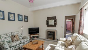 A living room with a sofa, a coffee table, a fireplace, a TV, and framed pictures on the wall.