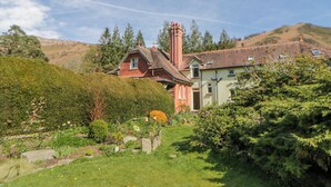A house with a garden, a chimney, and a hillside in the background.