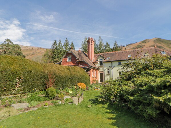 Une maison avec un jardin, une cheminée et une colline en arrière-plan.