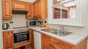 A kitchen with wooden cabinets, a microwave, a stove, a sink, and a window with a view of a brick structure.