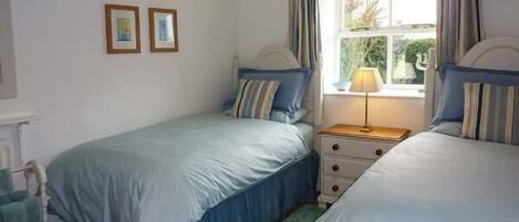 A bedroom with two beds, a nightstand, a lamp, and a window with curtains.
