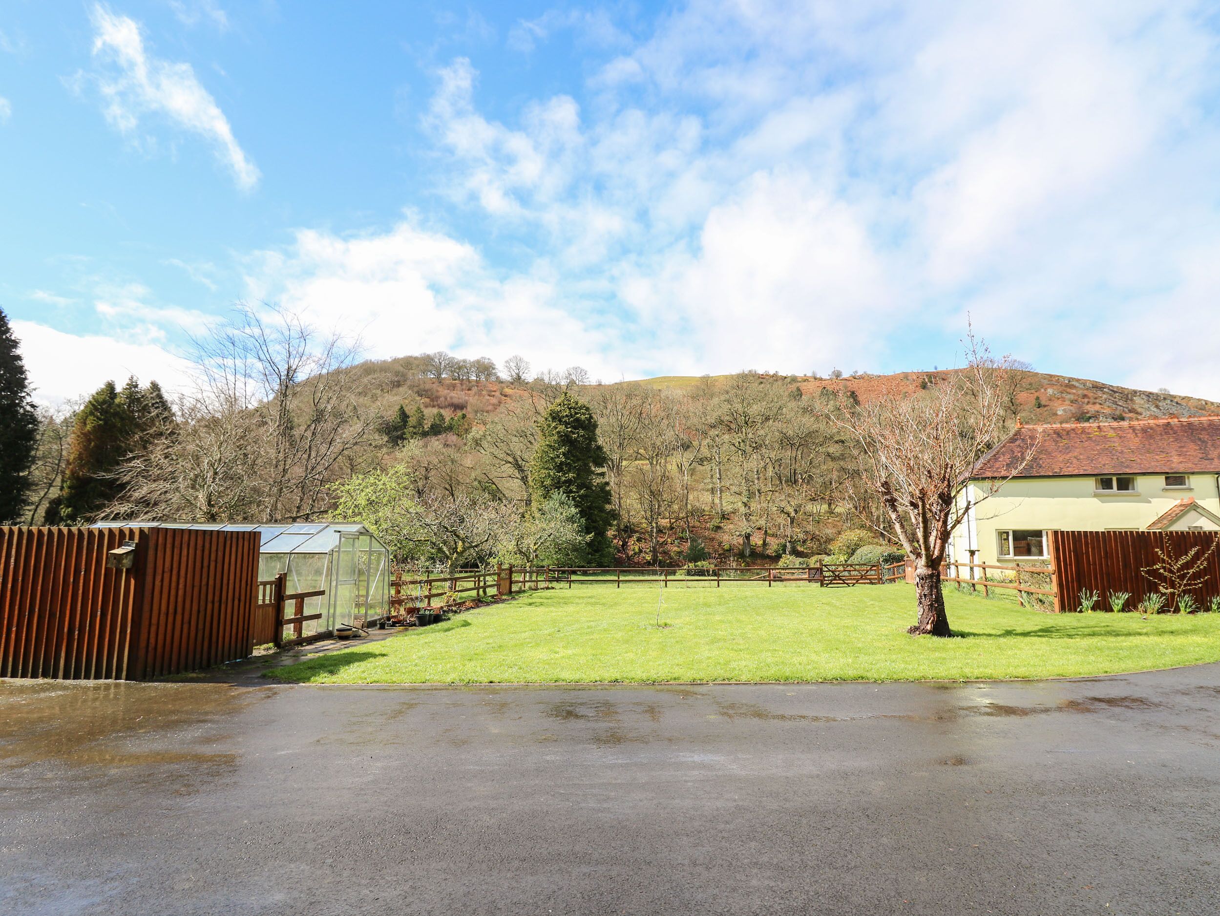 A residential property with a fenced yard, a greenhouse, and a house with a red-tiled roof.