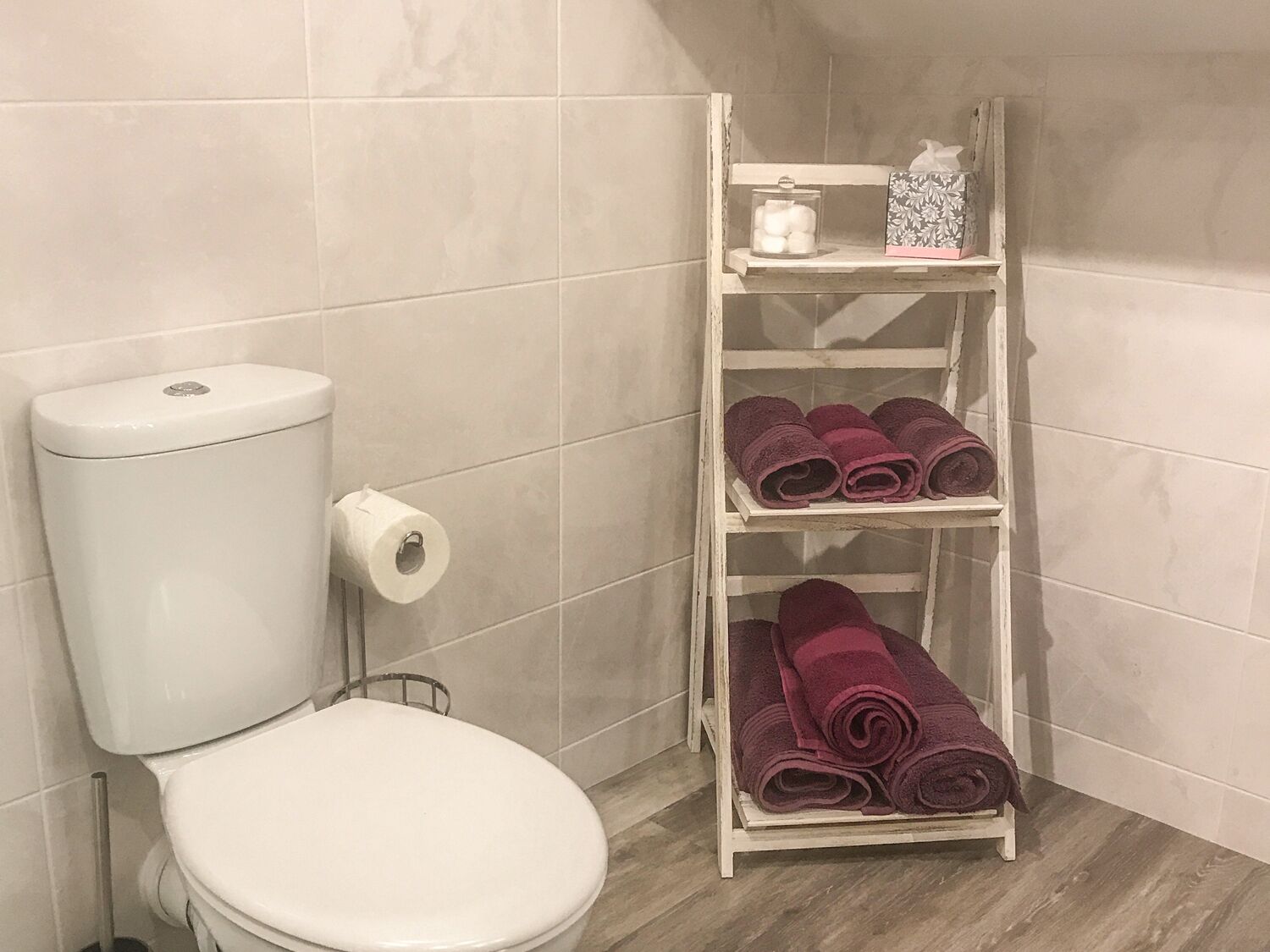 A bathroom with a toilet, a roll of toilet paper, and a shelf with towels.