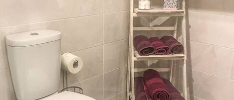 A bathroom with a toilet, a roll of toilet paper, and a shelf with towels.
