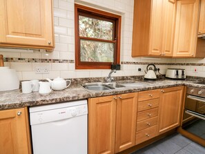 A kitchen with wooden cabinets, a Bosch dishwasher, a sink, a kettle, and a toaster.