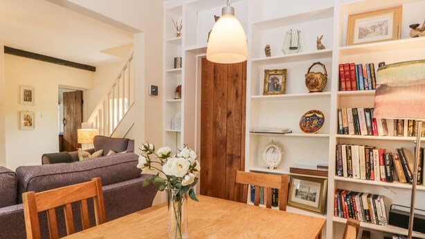Un salon chaleureux avec une table à manger en bois, un canapé et une bibliothèque remplie de livres et d’objets décoratifs.