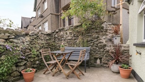 Un mur de pierre, un banc en bois et des plantes en pot dans une cour.