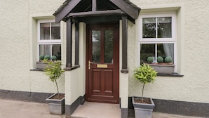 Une maison avec une porte d’entrée marron, deux fenêtres ornées de plantes en pot et un petit porche.