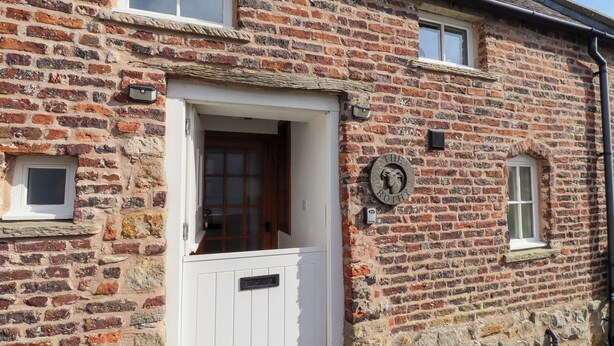 Un bâtiment traditionnel en briques, avec une porte blanche, une petite fenêtre et une enseigne indiquant « The Bothy ».