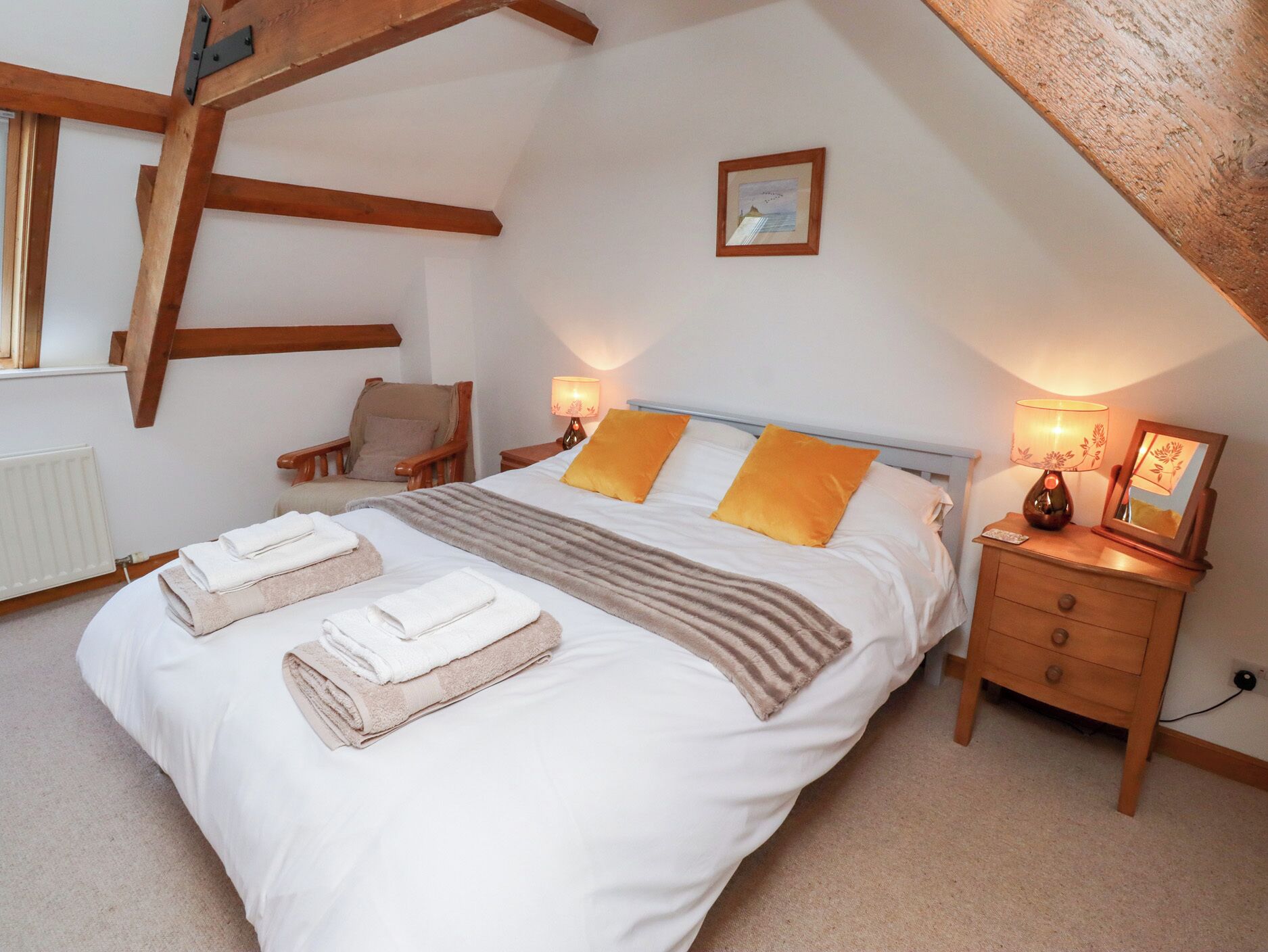 A bedroom with a large bed, two bedside tables, a chair, and a wooden ceiling beam.