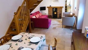 A dining area with a table set for four, a staircase, a red sofa, and a fireplace. - The Old Stable (Weston-super-Mare)