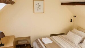 A neatly arranged bedroom with a bed, bedside table, lamp, and a small stool. - The Old Stable (Weston-super-Mare)