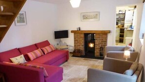 A living room with a red sofa, a grey armchair, a fireplace, and a television. - The Old Stable (Weston-super-Mare)