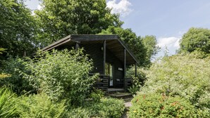 Un chalet rustique aux murs en bois, entouré d’une végétation luxuriante et accessible par un sentier de pierres.