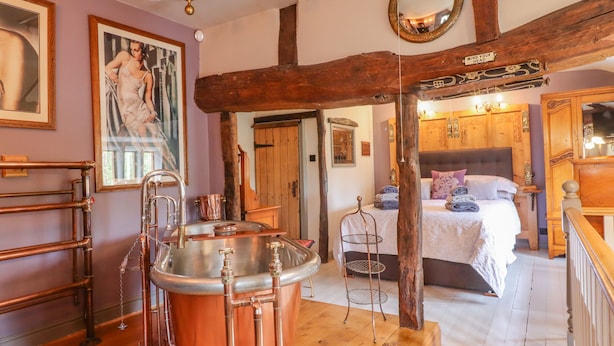 Une salle de bain rustique avec une baignoire en cuivre, des poutres en bois et un miroir ancien.