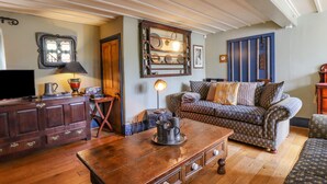 Un salon chaleureux avec une table basse en bois, un canapé à motifs et un téléviseur posé sur un meuble en bois.