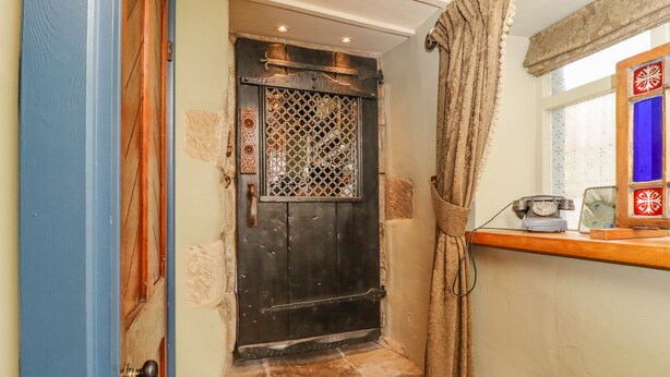 A narrow hallway with a wooden door, a small step, and a telephone on a shelf. - The Dairy (Keighley)