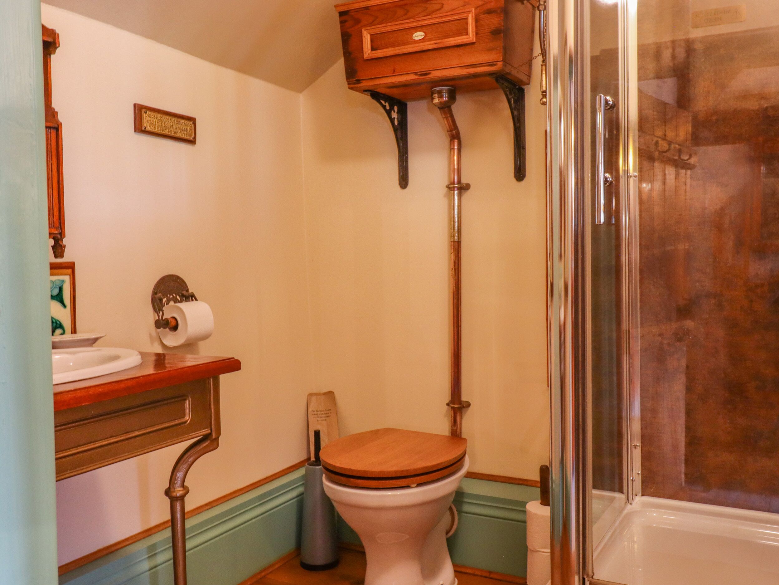Un baño con inodoro de madera, lavamanos blanco y cabina de ducha.