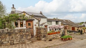 Une rangée de maisons traditionnelles en pierre, avec un mur de pierre au premier plan, une allée gravillonnée et un ciel dégagé.