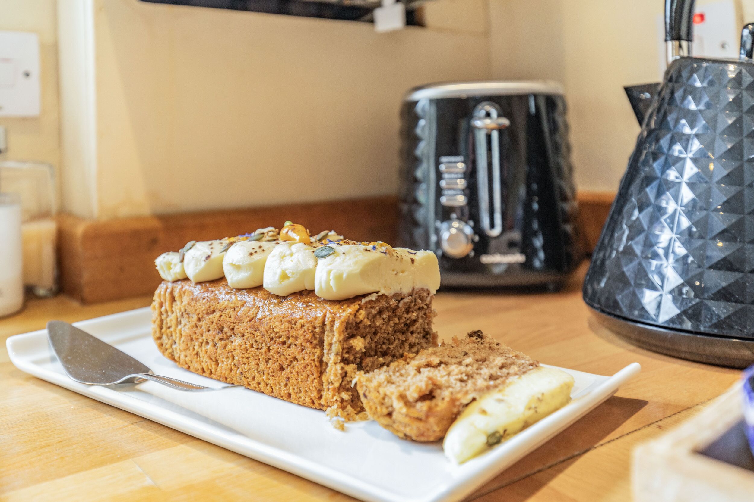 A loaf of banana bread on a white plate with a knife beside it, placed on a wooden table.