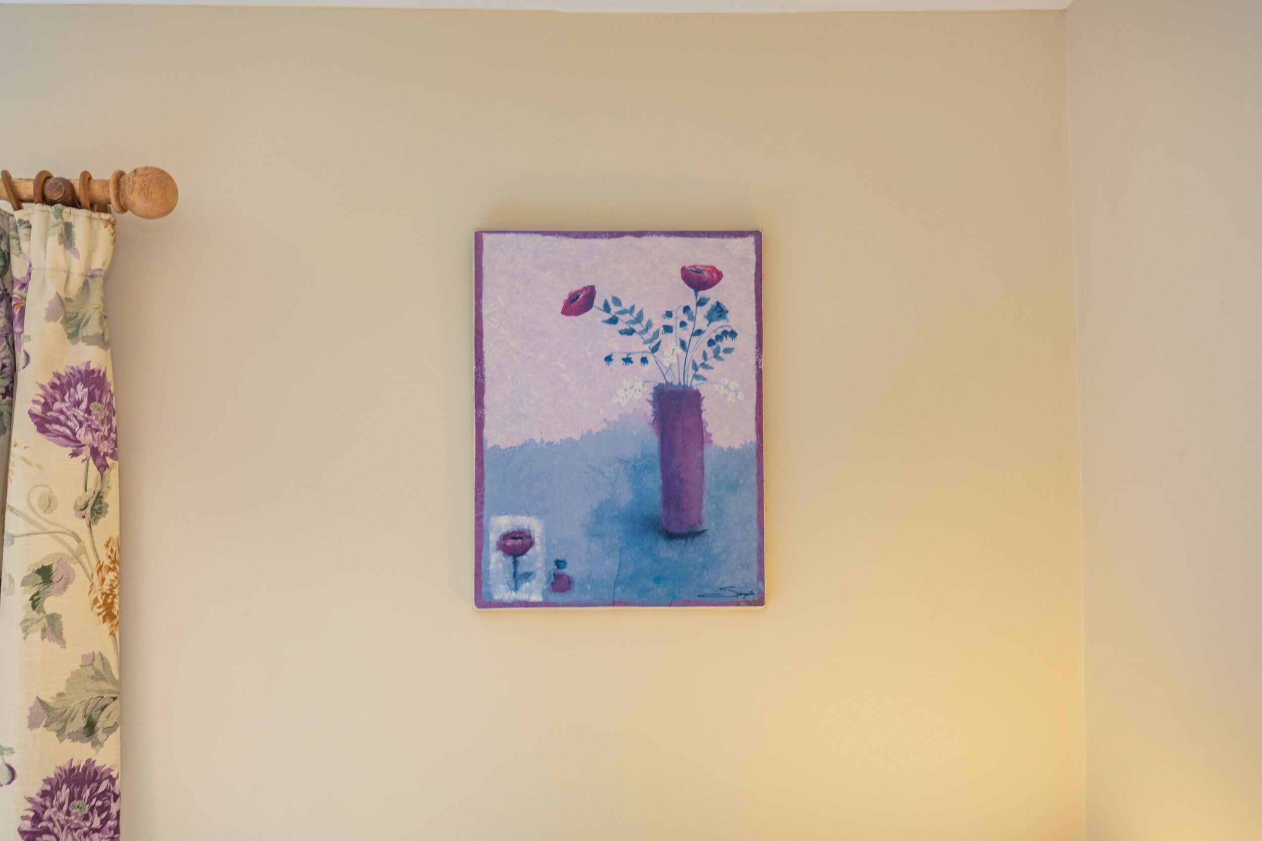En væg med et indrammet maleri af en vase med blomster.