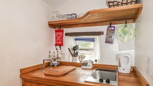 Cocina compacta con encimera de madera, un lavabo, una cafetera y una manta anti-fuego en la pared.