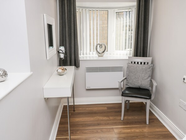 A room with a white desk, a chair, a radiator, a window with curtains, and a decorative item on the windowsill.