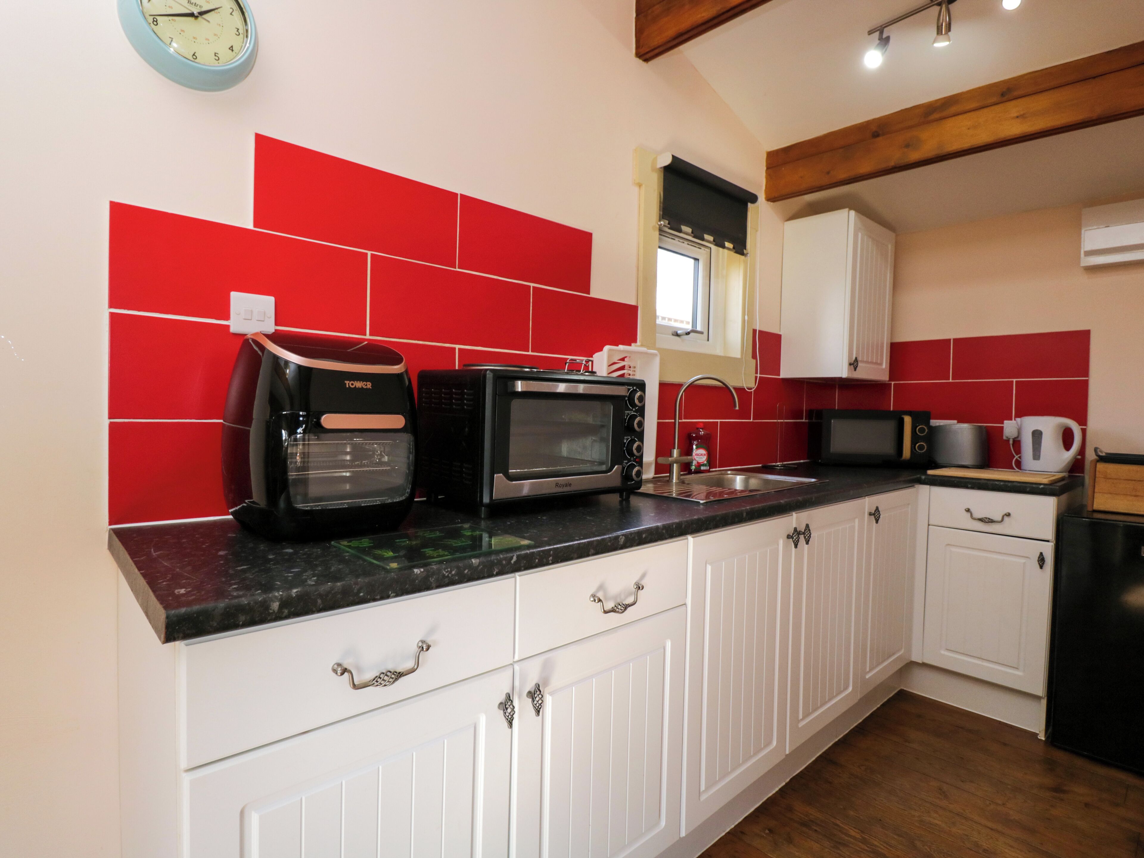 A kitchen with white cabinets, red tiles, a black countertop, a microwave, a toaster, and a sink.