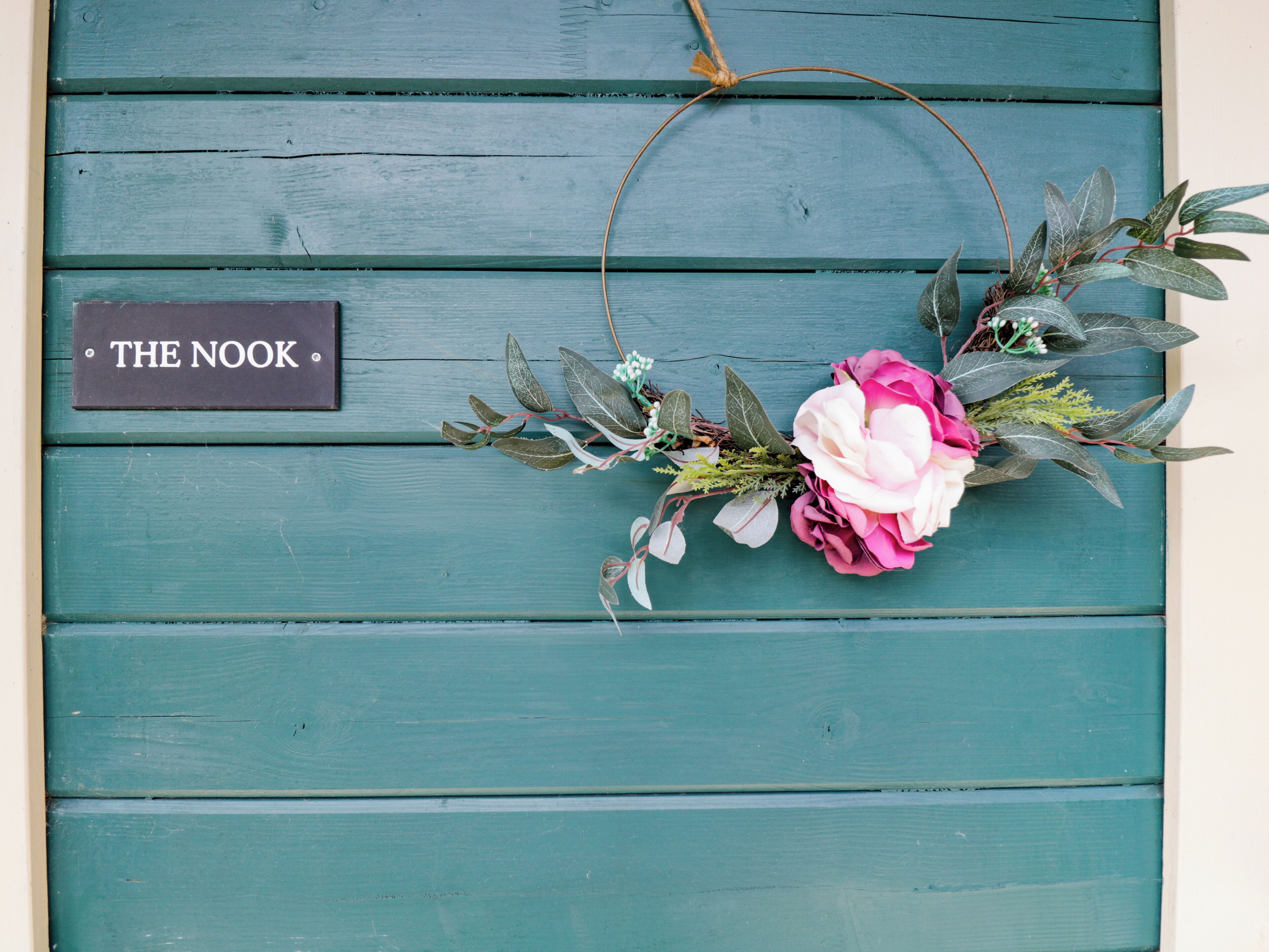 A teal wooden wall with a sign reading "THE NOOK" and a floral wreath.