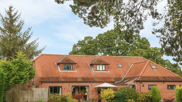 A two-story brick house with a red-tiled roof, a front porch, and a well-maintained lawn with picnic tables.