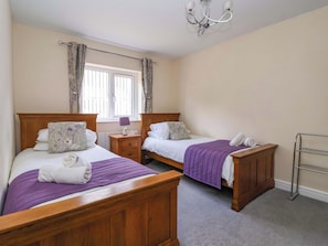 A bedroom with two wooden beds, a nightstand, a lamp, a radiator, and a window with curtains. - The Granary (York)