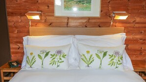 A bed with two pillows featuring botanical designs, a wooden headboard, and a framed landscape painting above. - Grasmere (Ulverston)