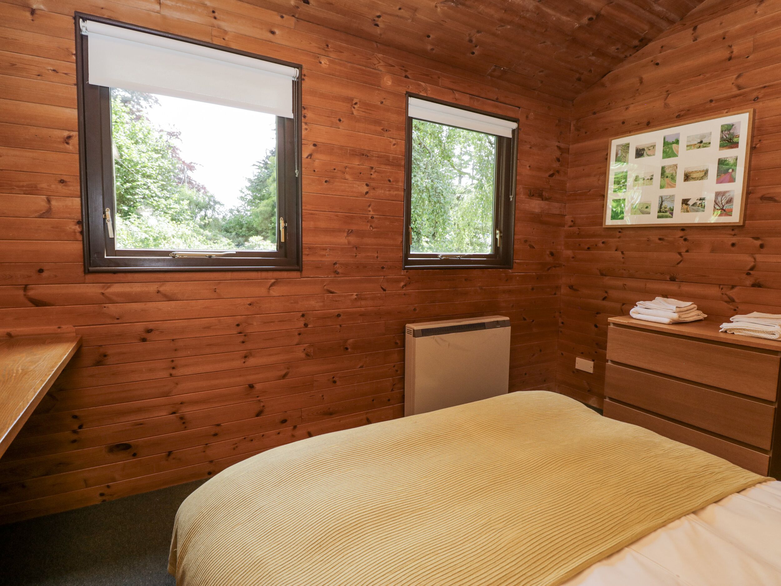 A wooden cabin room with two windows, a bed, a dresser, and a radiator.